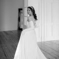 Load image into Gallery viewer, Woman in a white wedding dress standing in a room with wooden floors and white walls.