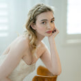 Load image into Gallery viewer, Woman in a white dress with a headband, sitting on a wooden chair indoors.