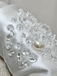 Load image into Gallery viewer, Close-up of a white bridal headband with clear crystals and a pearl on a neutral background