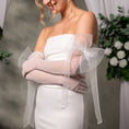 Load image into Gallery viewer, Woman wearing a white strapless dress with sheer gloves with a big bow, standing against a neutral background with flowers.