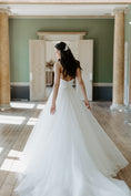 Load image into Gallery viewer, Woman in a white wedding dress standing in a room with columns and wooden floors.