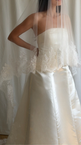 Load image into Gallery viewer, Bride wearing a white wedding dress with a lace veil against a white curtain background.