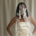 Charger l'image dans la visionneuse de la galerie, Bride wearing a white wedding dress with a lace veil against a white curtain background.