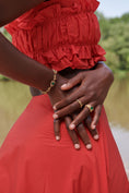 Load image into Gallery viewer, Person wearing a red dress with ruffled top and holding hands, with a blurred natural background. wearing gold bracelet and ring
