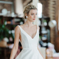 Load image into Gallery viewer, Woman wearing a white wedding dress with a slit in a blurred indoor setting