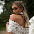 Load image into Gallery viewer, Woman wearing a white lace off-shoulder dress with a blurred natural background