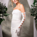 Load image into Gallery viewer, Woman wearing a white strapless dress and gloves with floral decorations in the background