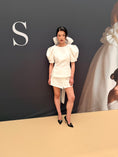 Load image into Gallery viewer, Woman in a white outfit standing on a beige carpet with a dark wall and 'S' logo in the background.
