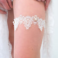 Load image into Gallery viewer, A white lace garter belt with pearl accents worn on a person's thigh, framed by white fabric.