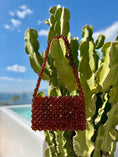 Load image into Gallery viewer, Red beaded bridal handbag on a cactus plant with a pool and blue sky in the background