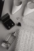 Load image into Gallery viewer, Jewelry including earrings, a ring, a bridal bag, and a small bottle on a textured surface.