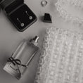 Load image into Gallery viewer, Jewelry including earrings, a ring, a bridal bag, and a small bottle on a textured surface.