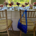 Load image into Gallery viewer, Decorated table with flowers and a blue beaded bridal bag in an outdoor setting.