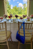 Load image into Gallery viewer, Decorated table with flowers and a blue beaded bridal bag in an outdoor setting.