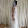 Charger l'image dans la visionneuse de la galerie, White lace veil and wedding dress on a wooden floor with a plain white wall background