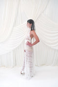Load image into Gallery viewer, A woman wearing a sleeveless white lace bridal gown and a crystal mini bridal veil stands in profile against a draped white fabric backdrop.