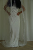 Load image into Gallery viewer, Person wearing a white wedding dress with a long veil in front of white curtains.