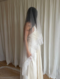 Load image into Gallery viewer, Bride wearing a white wedding dress with a lace veil against a white curtain background.