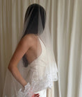 Charger l'image dans la visionneuse de la galerie, person in a wedding dress with a long lace trim veil against a curtain backdrop.