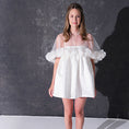 Load image into Gallery viewer, A woman modeling a short white dress with a 3d flower tulle bridal cape standing against a dark textured studio wall.