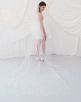 Load image into Gallery viewer, A woman wearing a sheer white bridal veil with delicate bow details and a short white slip dress, standing in front of draped white fabric.