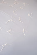 Load image into Gallery viewer, A sheer white tulle veil with multiple small white ribbon bows scattered across a light gray background.