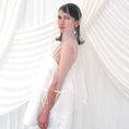 Load image into Gallery viewer, A woman wearing a sheer white bridal veil with delicate bow details and a short white slip dress, standing in front of draped white fabric.