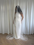 Load image into Gallery viewer, Person wearing a white wedding dress with a long pearl veil against a plain background