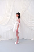 Load image into Gallery viewer, A young girl modeling a short white slip dress with a tulle petal bridal cape and white pointed-toe heels, standing against a draped white fabric backdrop.
