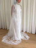 Load image into Gallery viewer, White lace veil and wedding dress on a wooden floor with a plain white wall background