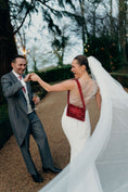 Load image into Gallery viewer, Man and woman in wedding attire standing outdoors with trees and lights in the background wearing bridal bag