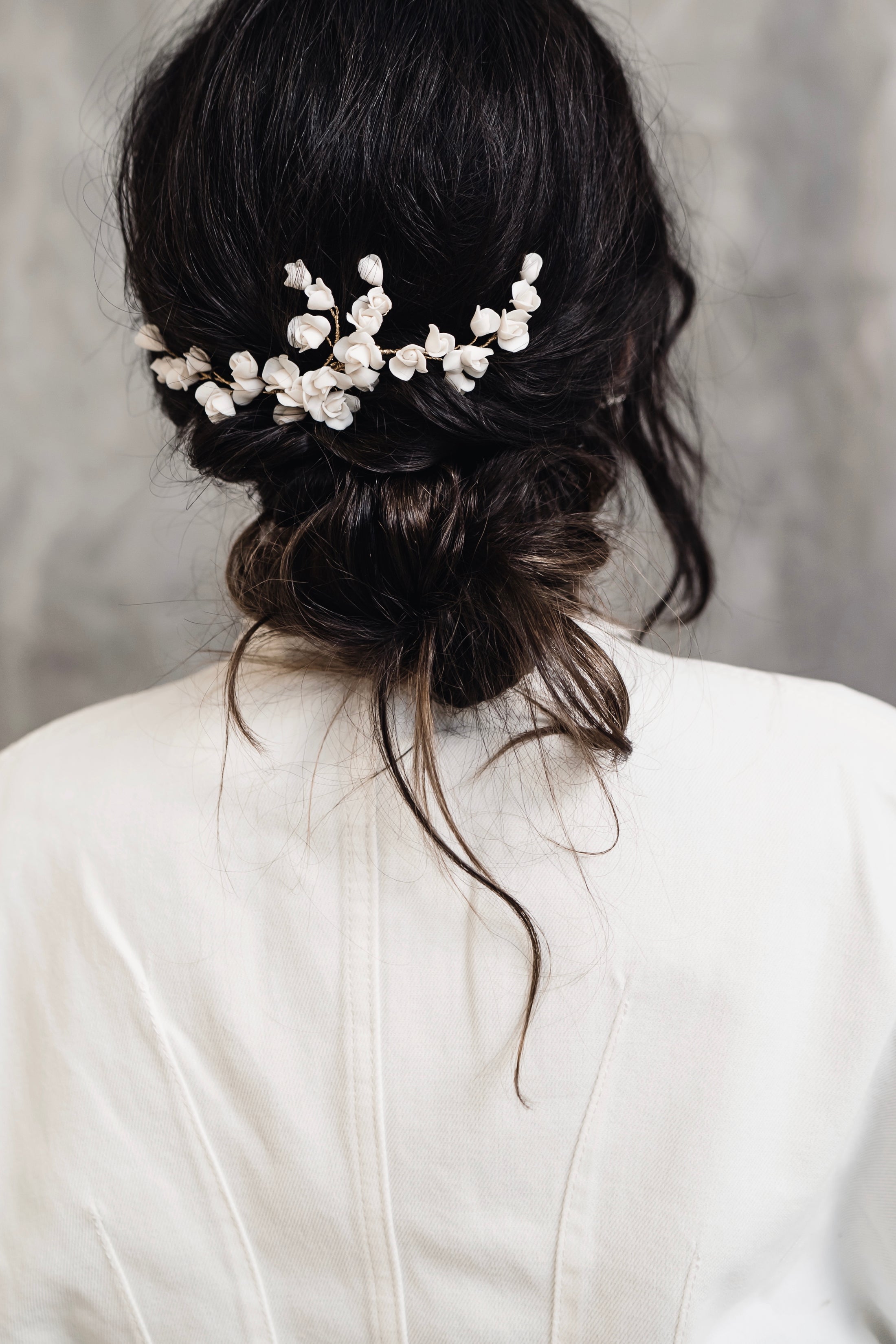 Back view of a person with a decorative hairpiece wearing a white top against a gray background