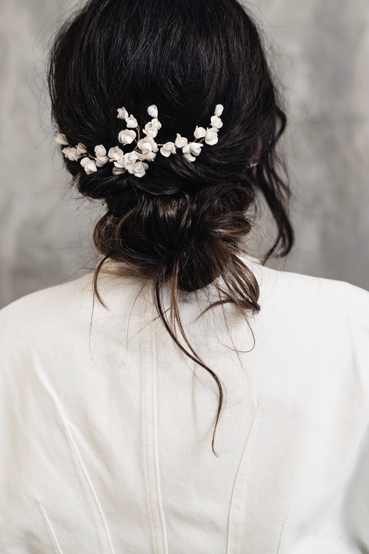Back view of a person with a decorative hairpiece wearing a white top against a gray background