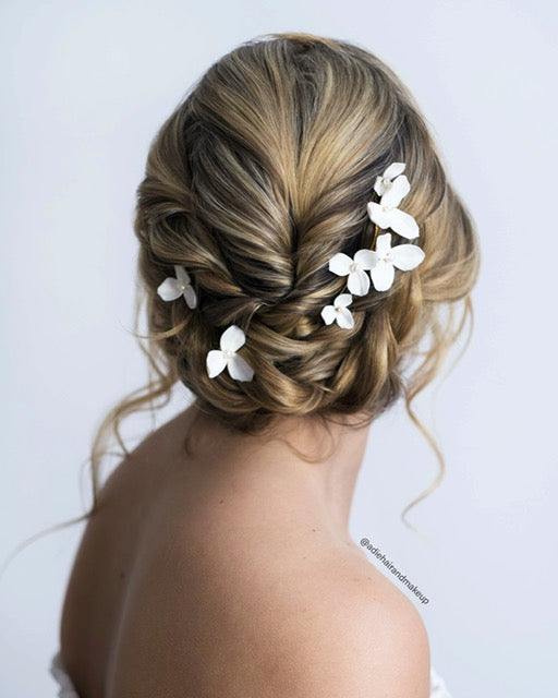 Updo hairstyle with floral hairpins on a plain background