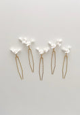 Load image into Gallery viewer, Set of five gold hairpins with white floral attachments on a light gray background
