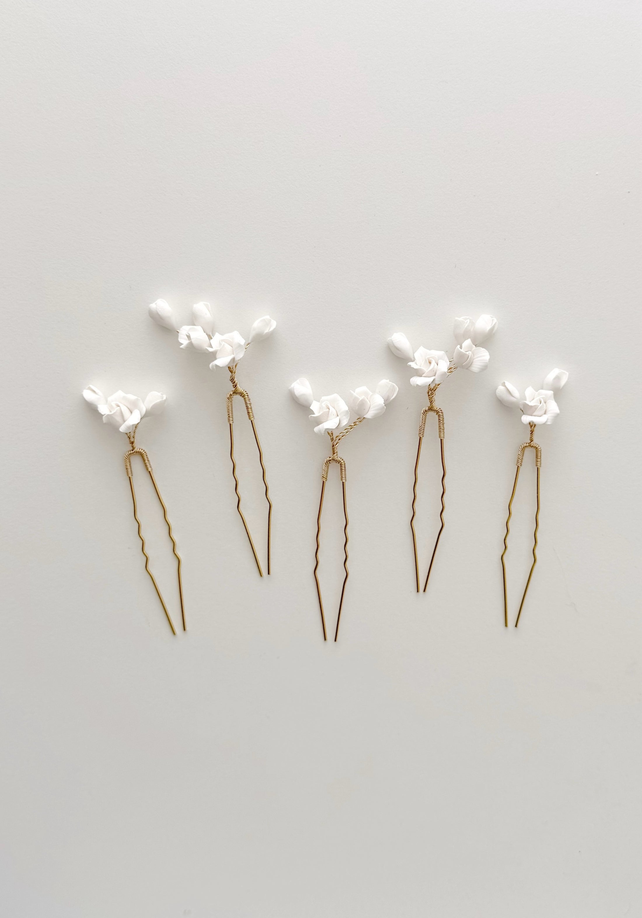 Set of five gold hairpins with white floral attachments on a light gray background