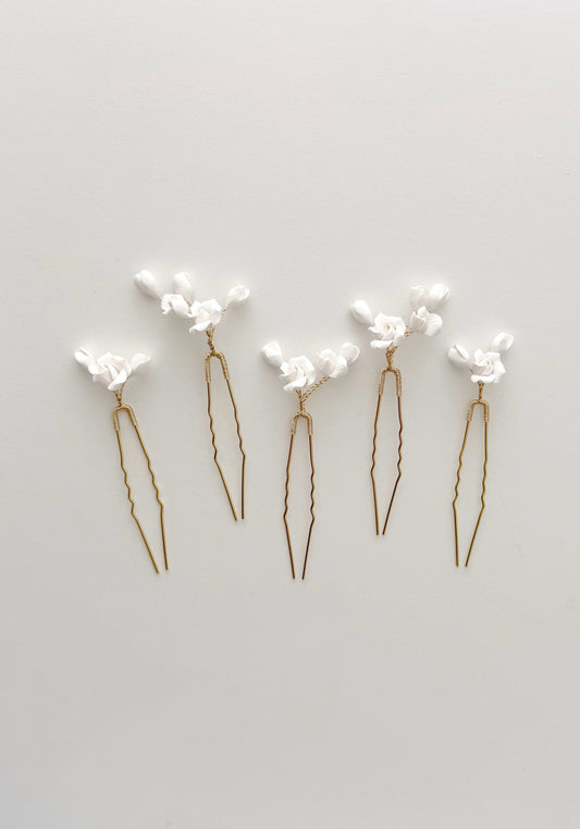Set of five gold hairpins with white floral attachments on a light gray background