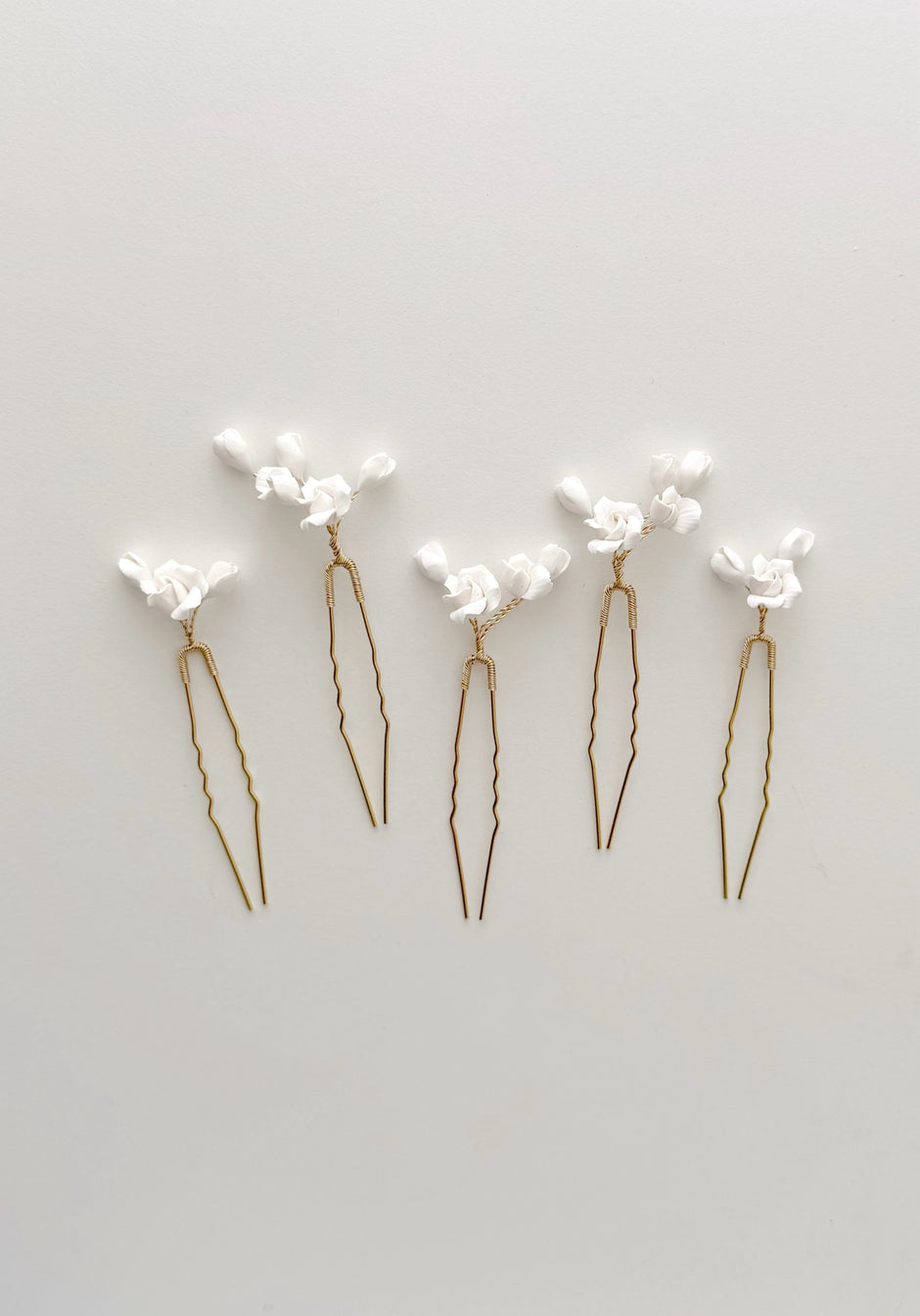 Set of five gold hairpins with white floral attachments on a light gray background