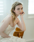 Load image into Gallery viewer, Woman in a white dress with a headband, sitting on a wooden chair indoors.
