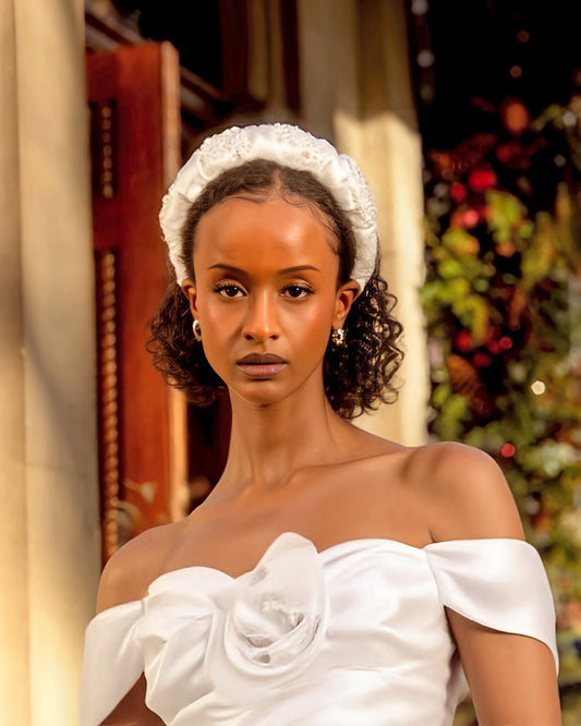 Woman wearing a white off-shoulder dress with a decorative bridal headband against a festive background.