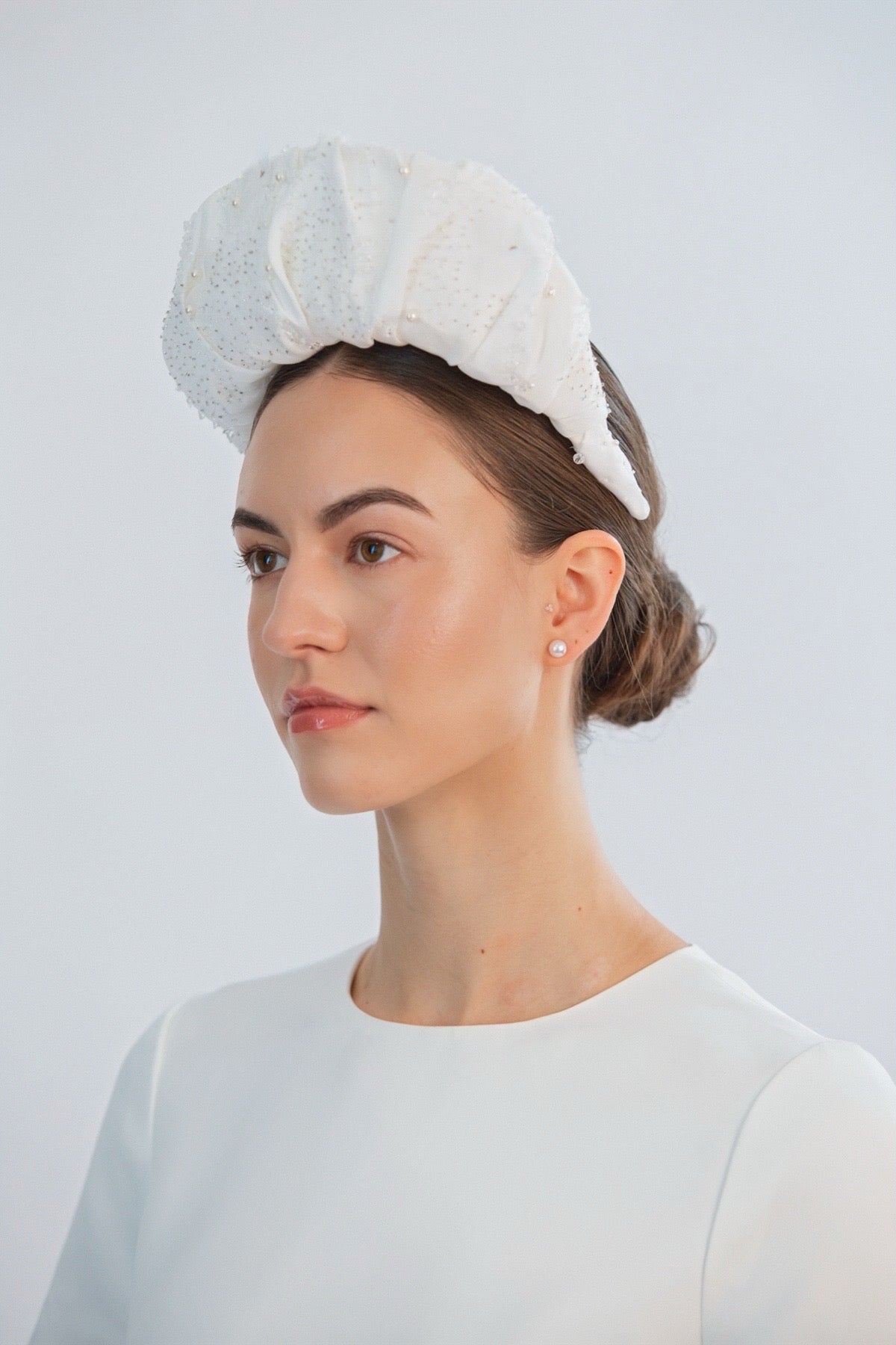 Woman wearing a white bridal headband against a light grey background