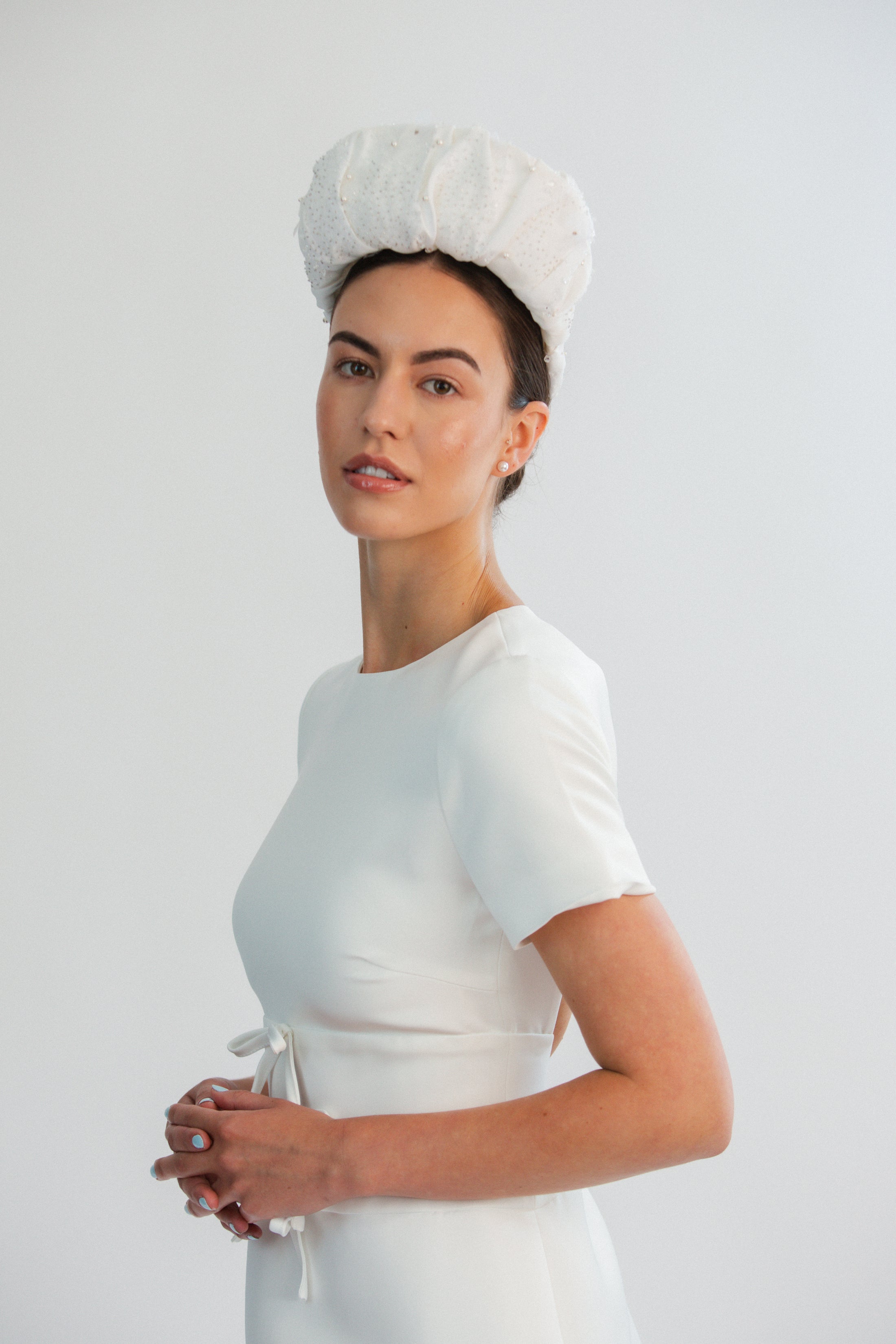 Woman wearing a white bridal headband against a light grey background
