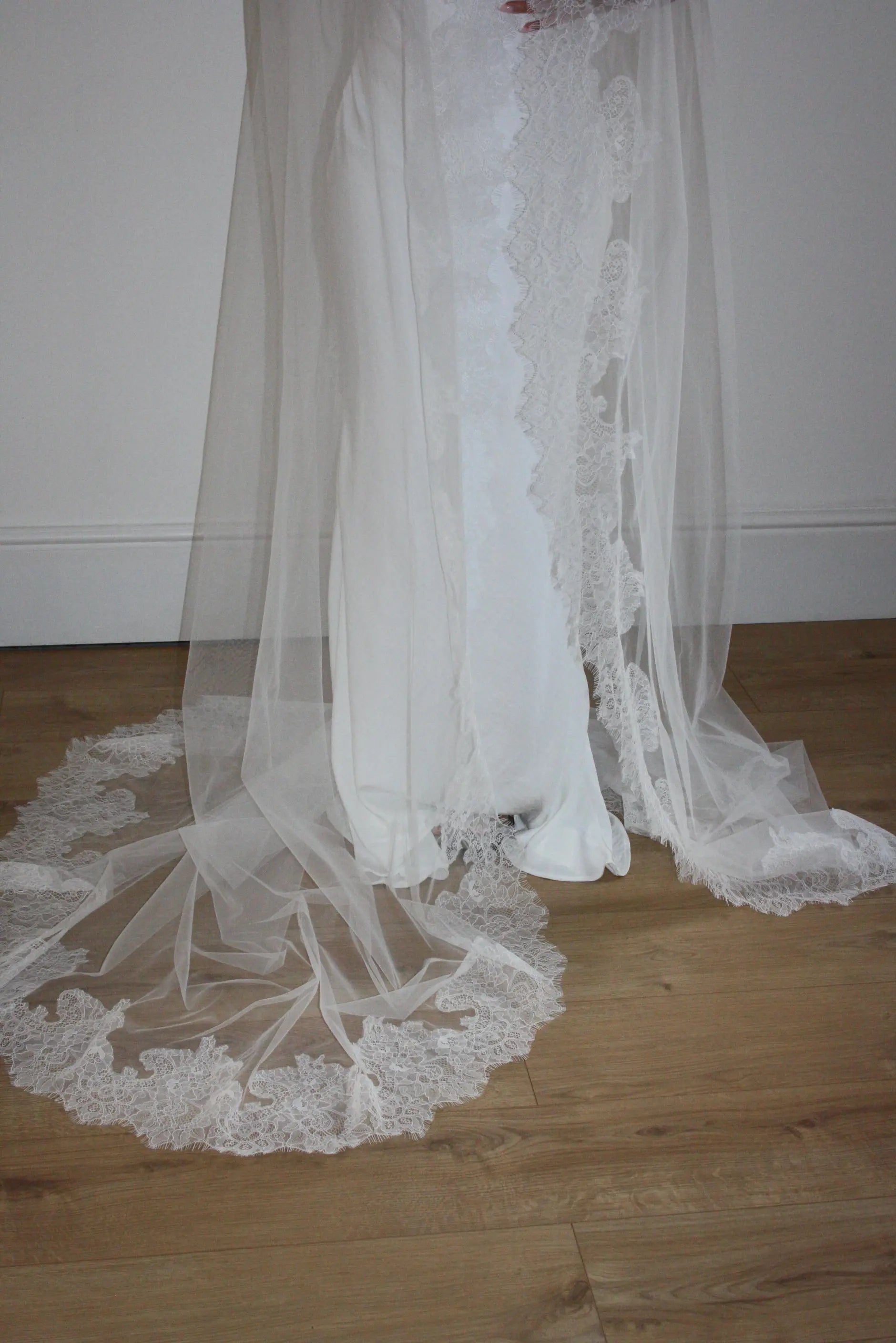 White lace veil and wedding dress on a wooden floor with a plain white wall background