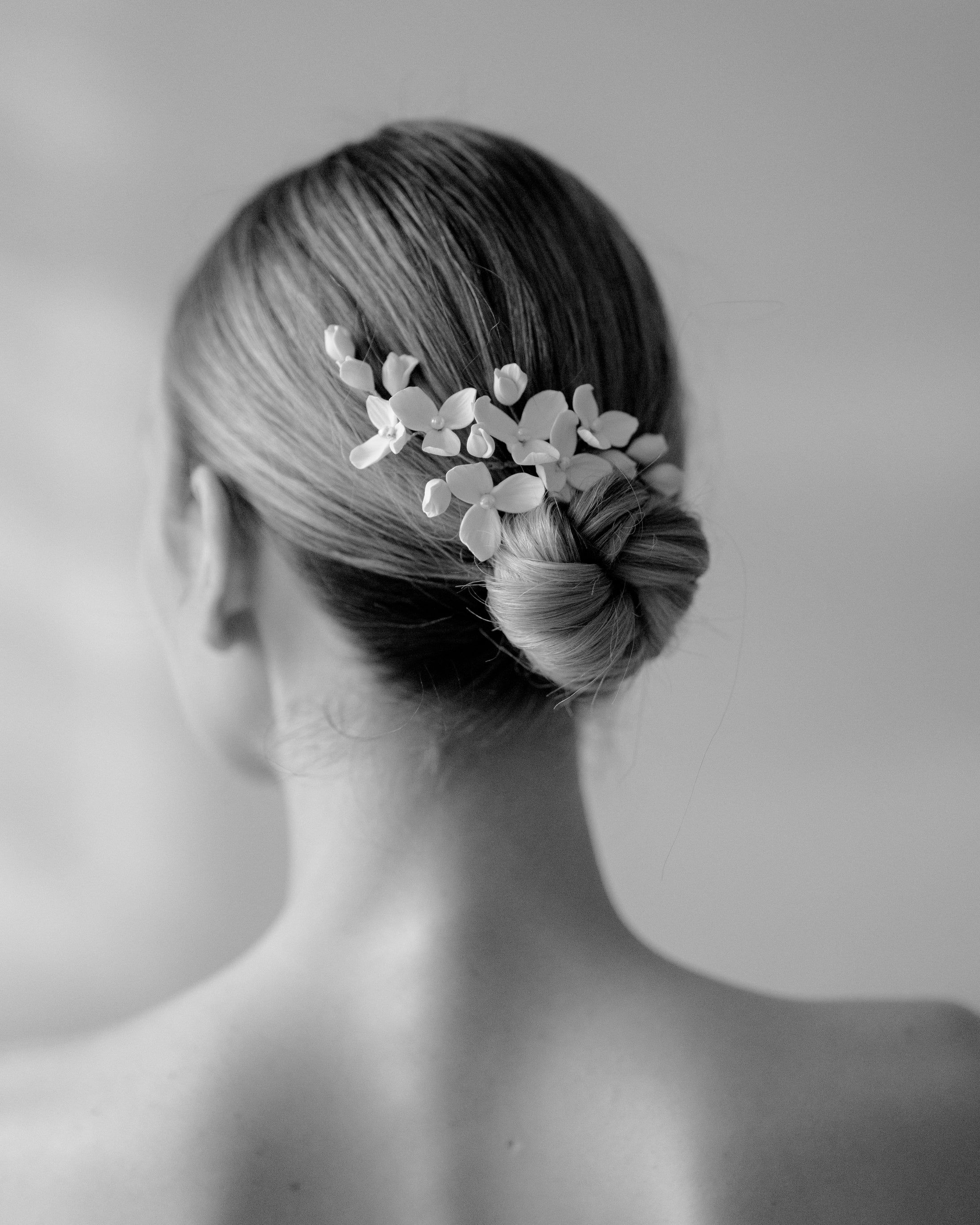Person with a stylish hair bun adorned with floral hairpiece against a plain background