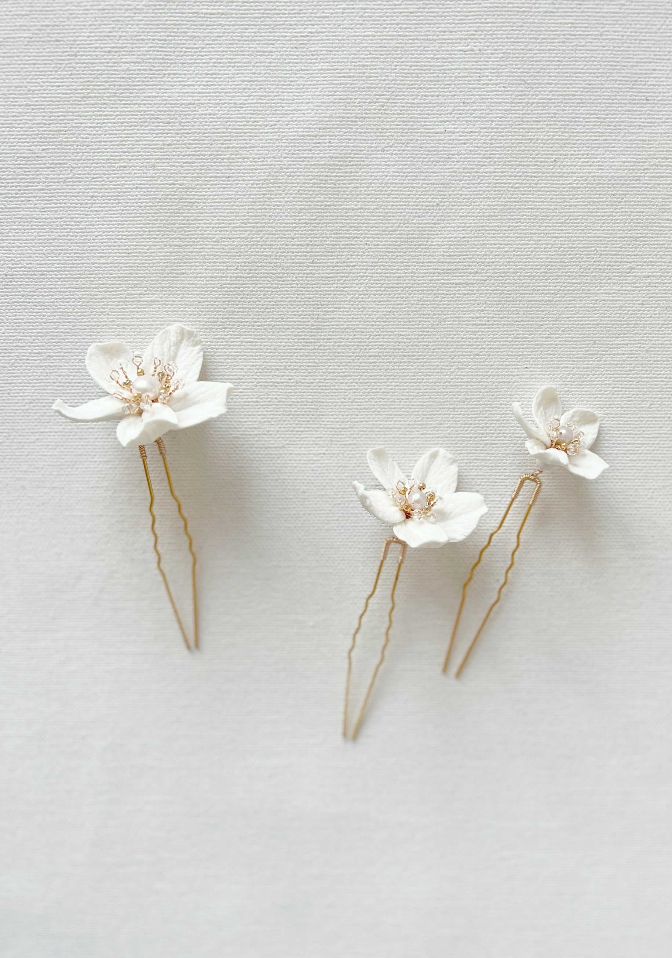 Two white floral hairpins with gold accents on a light gray background