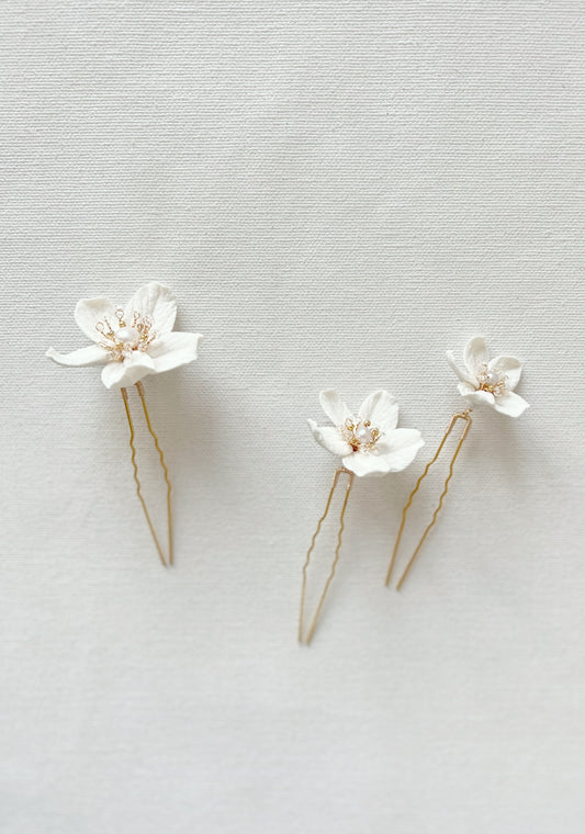 Two white floral hairpins with gold accents on a light gray background