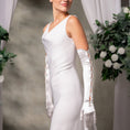 Load image into Gallery viewer, Woman in a white wedding dress with long gloves standing against a neutral background with floral decorations.
