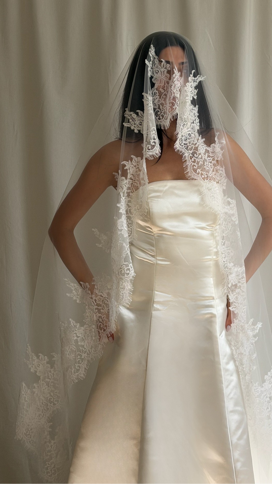 Bride wearing a white wedding dress with a lace veil against a white curtain background.