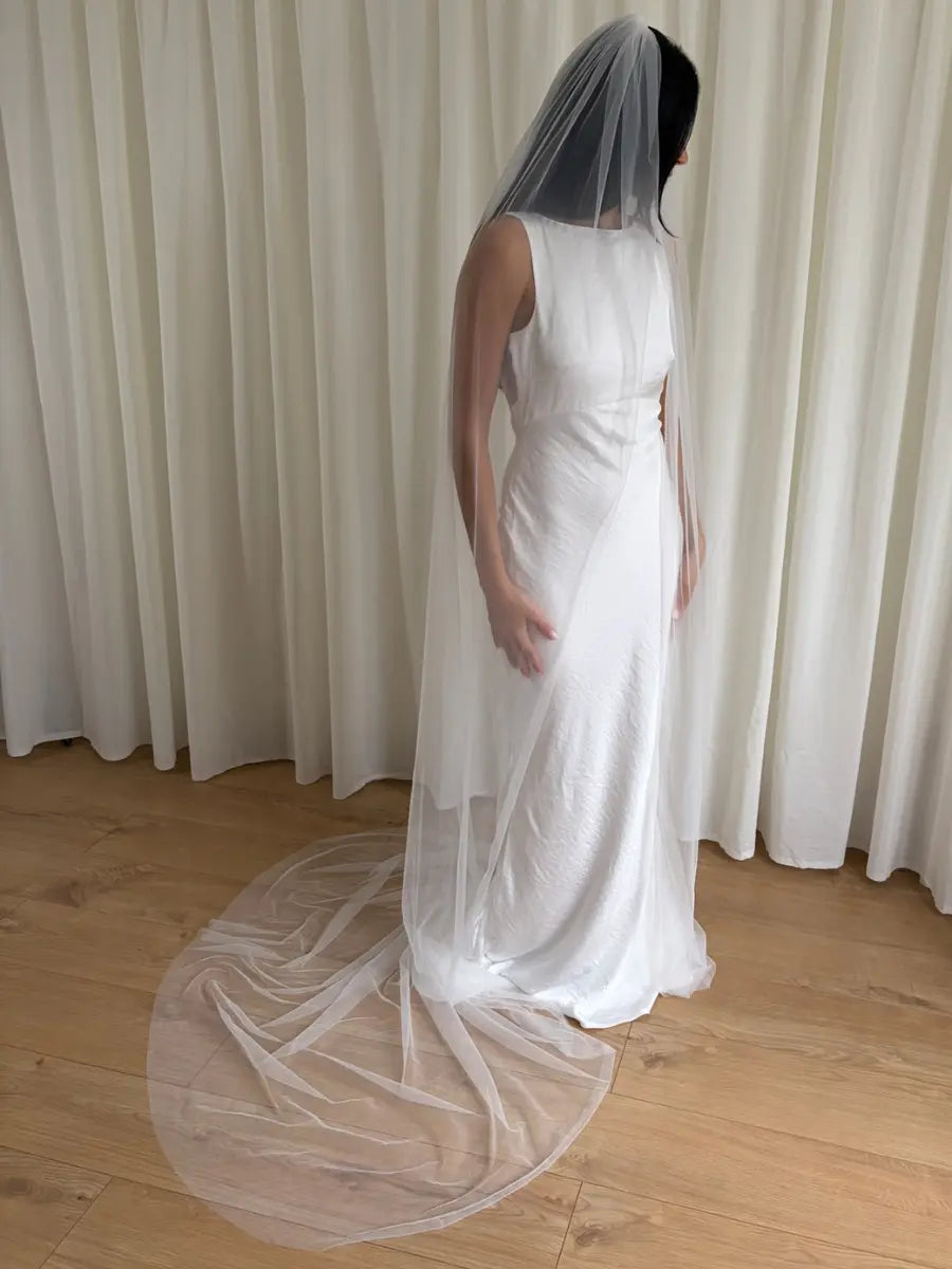 Person wearing a white wedding dress with a long plain veil against a plain background
