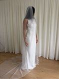 Load image into Gallery viewer, Person wearing a white wedding dress with a long plain veil against a plain background

